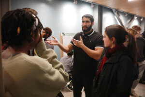 Farhan Alemi stands beside a research poster while explaining his project to a small group of students.