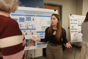 Lillie Burbulis stands beside a research poster while presenting her biology project.