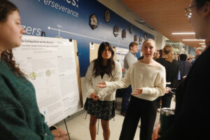 Students stand in front of a research poster about algae composition and freshwater species while presenting their project.
