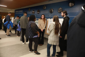 A group of students stands near research posters while discussing projects in the Jepson Science Center lobby.