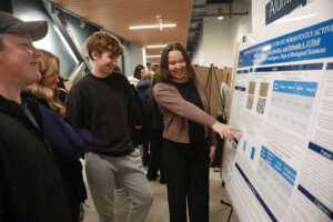 A student researcher presents a biology poster while explaining her project to attendees at the Jepson Science Center symposium.
