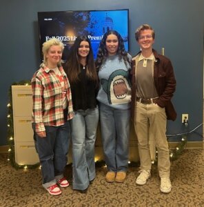 Four student interns, one junior and three seniors, stand together in the University Communications office during a video production showcase.