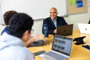 Photo of the Director of the Center for AI and the Liberal Arts Anand Rao seated at a table with students, laptops