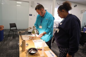 A man and a woman stand at a table holding pieces of paper beneath a lightbulb.