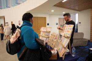 A man stands behind the counter while a woman browses for merchandise, including books and stickers.