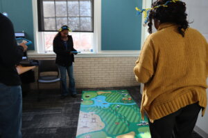 Conference participants maneuver a robotic item across a rug imprinted with a terrain design.