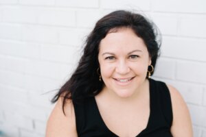 Jessica McCaughey '01 smiling against a white brick background. 