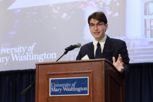 A student at a podium with a University of Mary Washington sign.