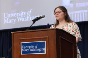 A student at a podium with a University of Mary Washington sign.