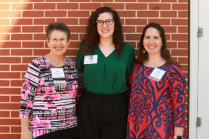 Two donors and a student recipient standing in front of a brick wall.