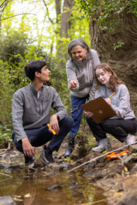 A photo of two students with their faculty mentor working outdoors in the field.