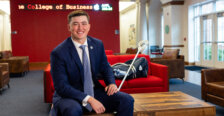 Photo of Jay Hooker in a business suit holding a lacrosse stick in the lobby of the College of Business