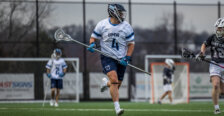 Photo of a Jay Hooker in a white jersey playing lacrosse for UMW holding a lacrosse stick.