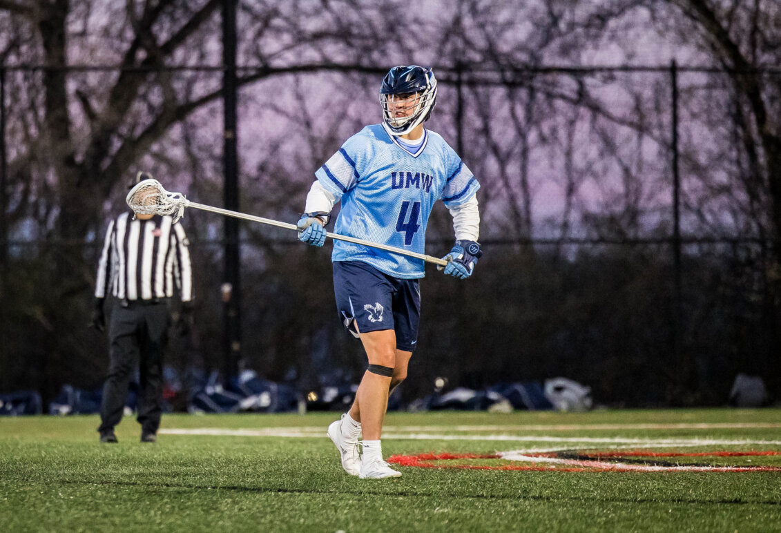 Photo of a Jay Hooker in a light blue jersey playing lacrosse for UMW holding a lacrosse stick.