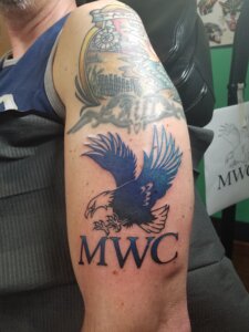 Photo of an arm with a tattoo that includes an eagle and the letters MWC.