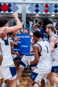 Photo of UMW basketball players celebrating and placing their team name on the tournament bracket.