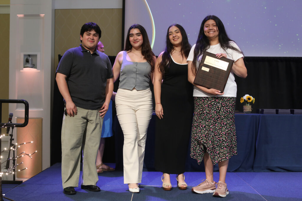 Four students pose holding an award