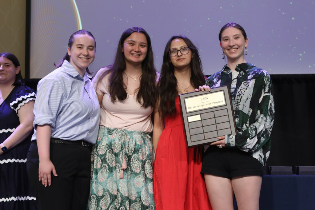 Four students stand side by side holding an award