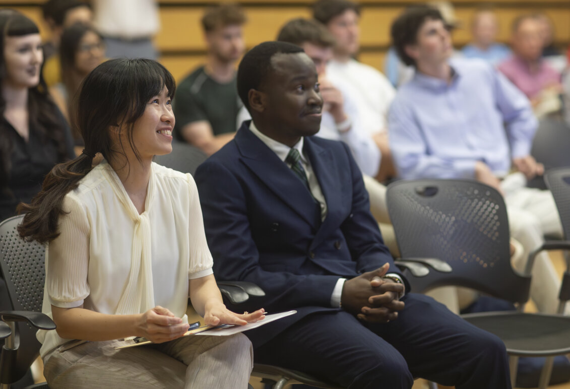 A woman and a man sit side-by-side watching presentations