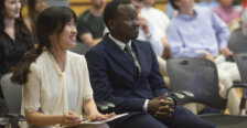 A woman and a man sit side-by-side watching presentations