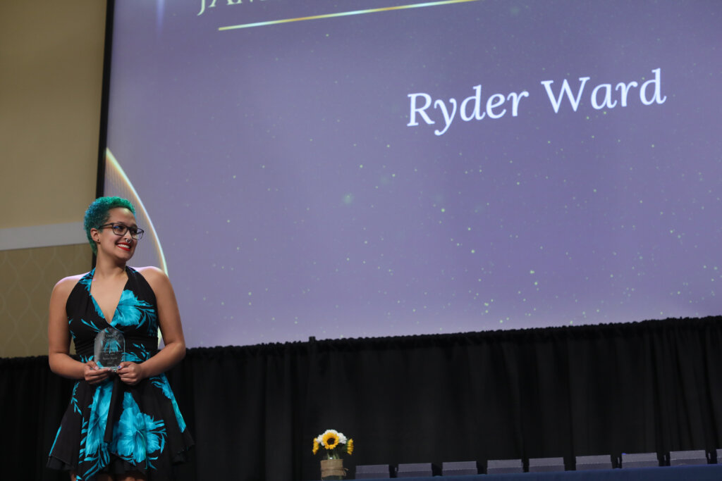 A student stands onstage holding an award