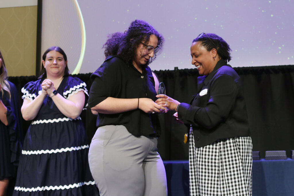 Three women, one of whom is accepting an award, stand onstage.