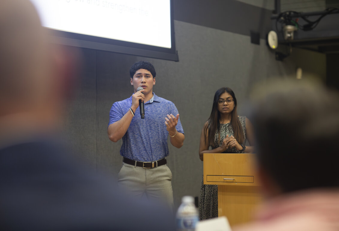 A girl stands behind a podium and beside a boy talking on a microphone