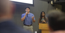 A girl stands behind a podium and beside a boy talking on a microphone