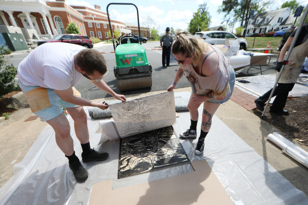 A professor and a student check the student's print with the rented steamroller in the background. 