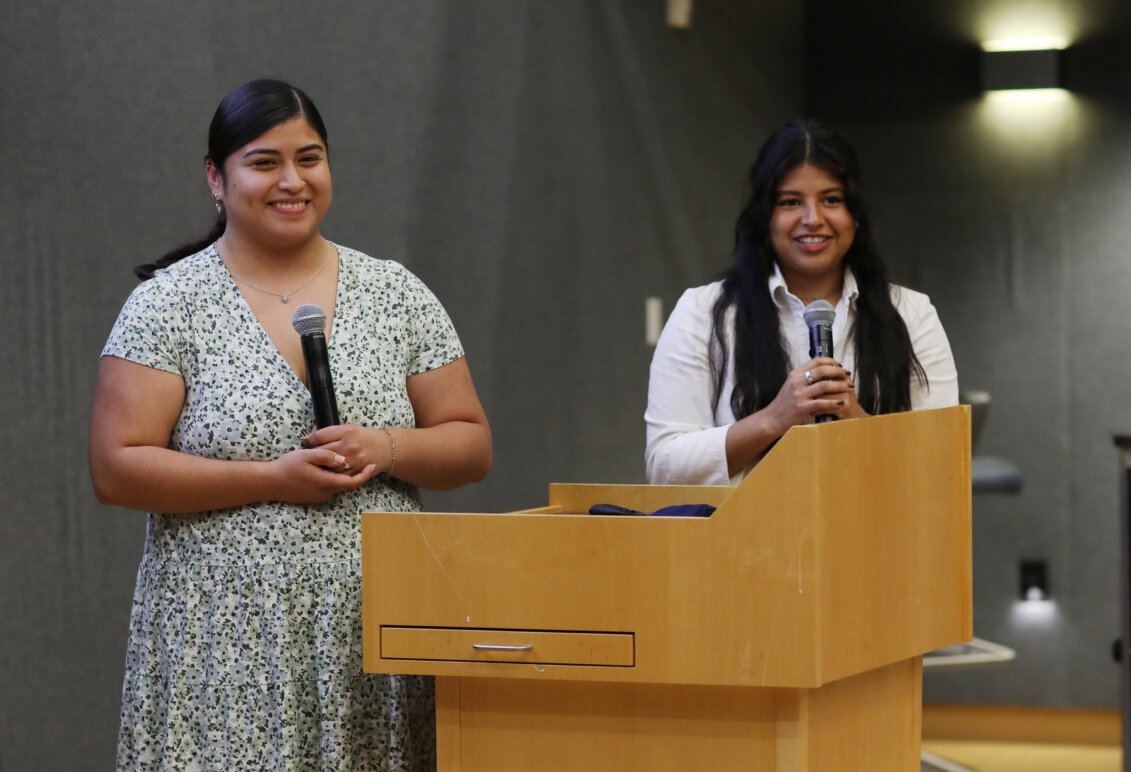 Two girls stand behind a podium with microphones in their hands