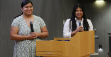 Two girls stand behind a podium with microphones in their hands