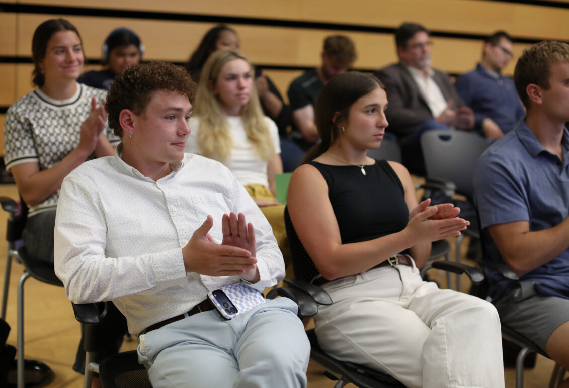 A boy and a girl sit in the front row of an audience that is clapping