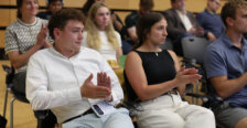 A boy and a girl sit in the front row of an audience that is clapping