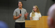 Two girls stand behind a podium, while one speaks into a microphone