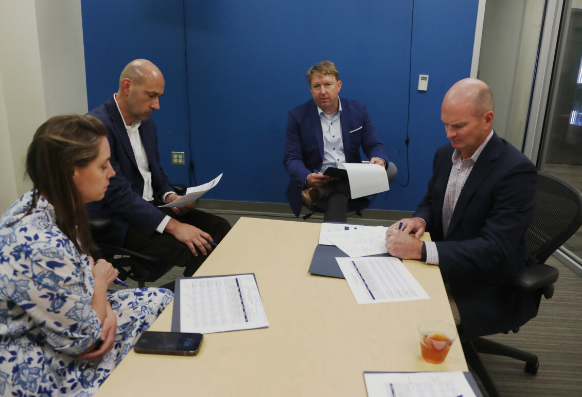 A woman and three men sit around a table with papers in front of them