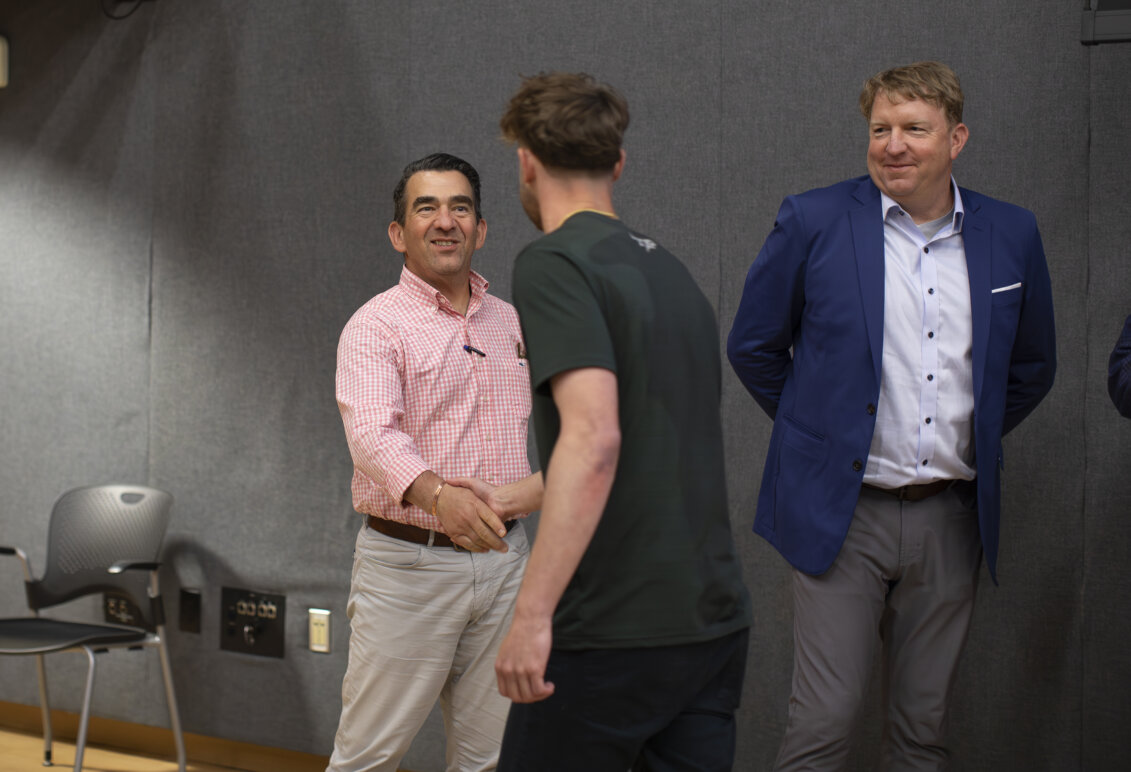 Two men shake hands while another looks on