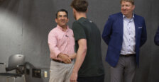 Two men shake hands while another looks on