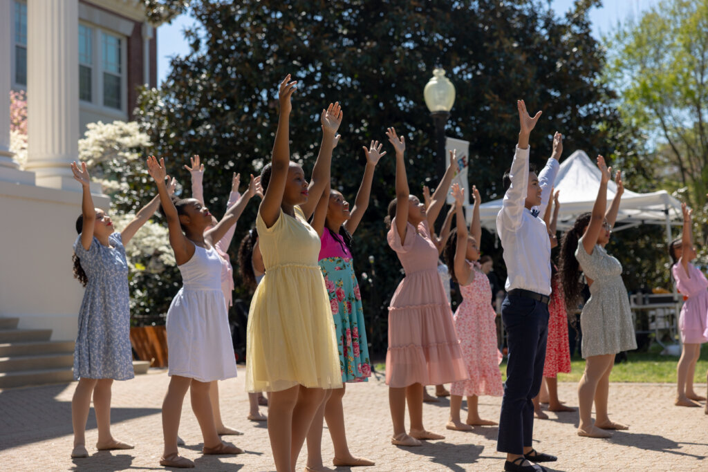 Several dancers in pastel shades reach their arms upward during a performance