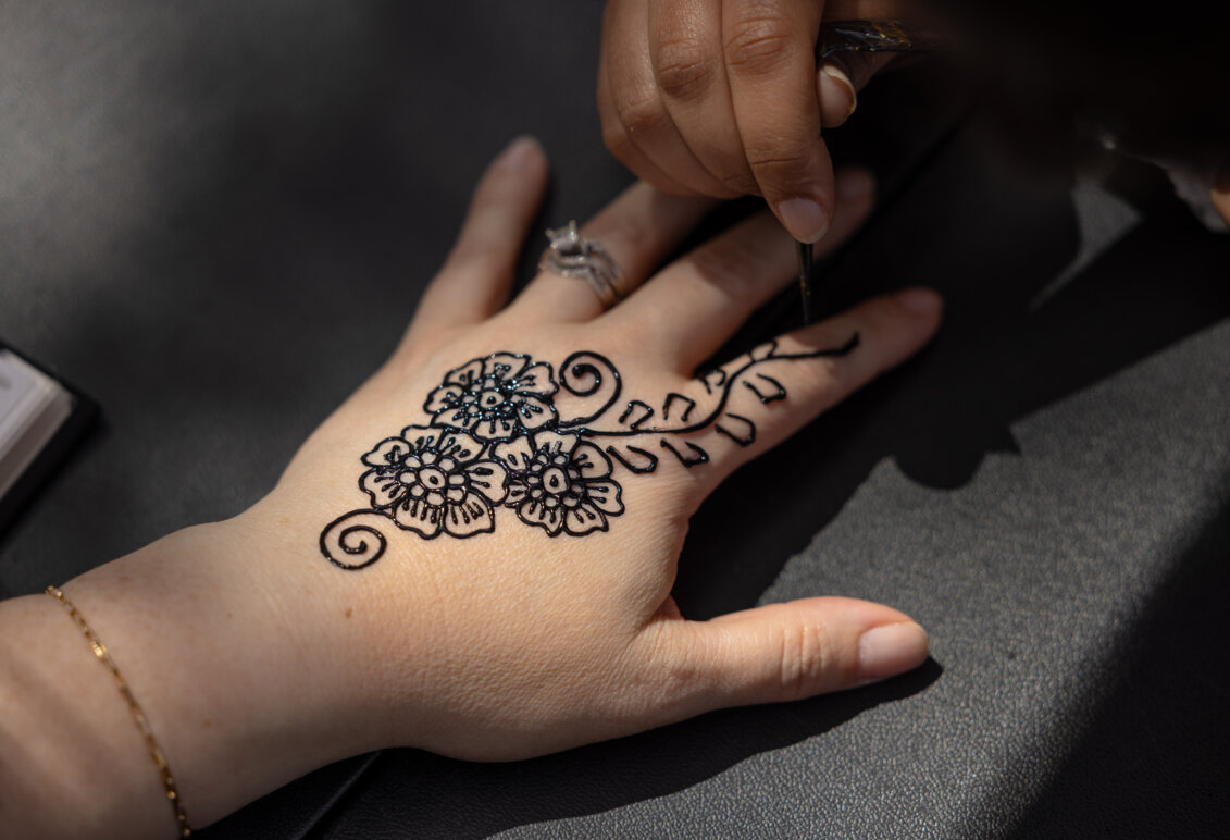 Photo of two hands, with one painting henna designs on the other
