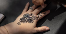 Photo of two hands, with one painting henna designs on the other