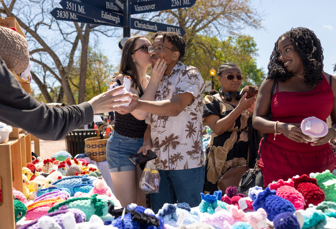 A girl kisses a boy on the cheek while some other people shop for trinkets