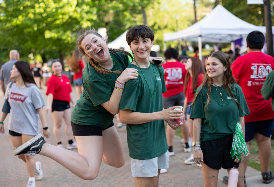 a girl jumps up on the shoulders of a guy before a crowd in the background