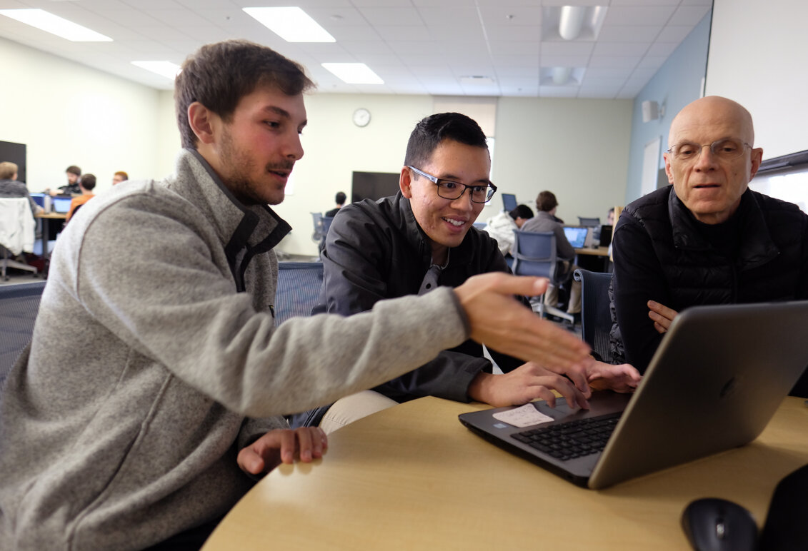 Two students show a professor their work on a laptop computer in 2017