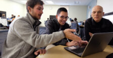 Two students show a professor their work on a laptop computer in 2017