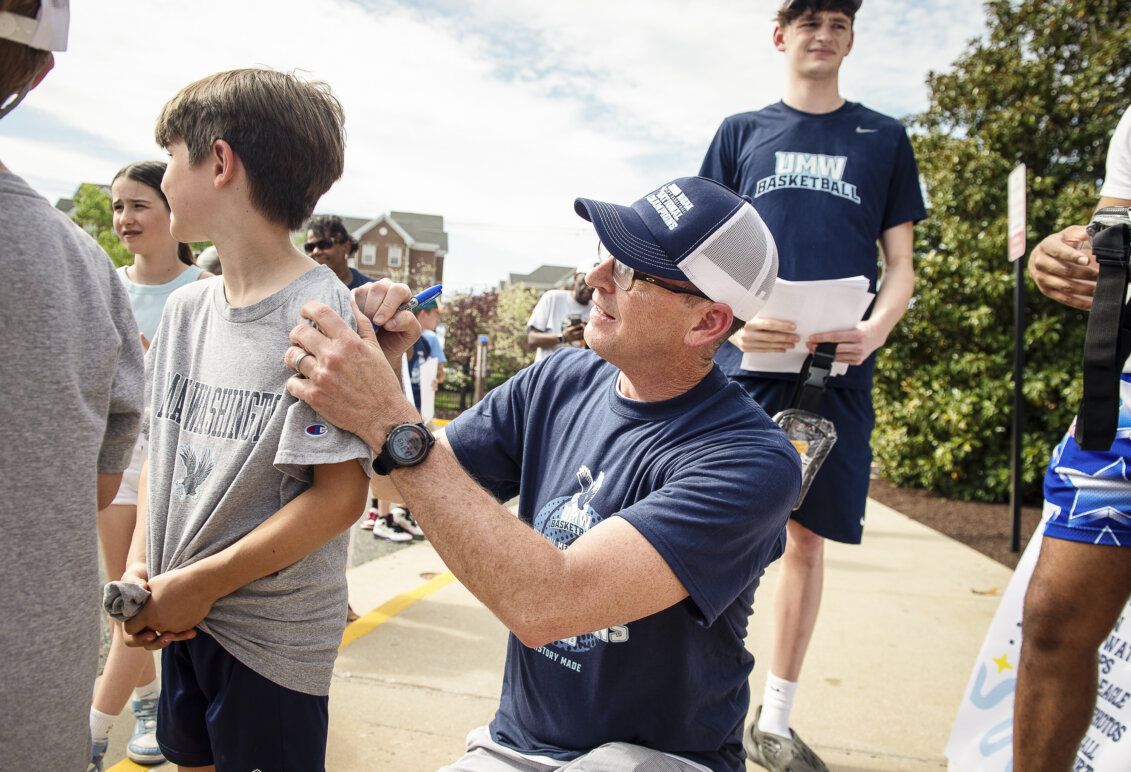 A basketball coach signs an autograph, using a child's back for a surface to write on