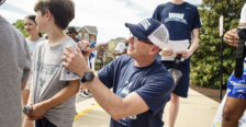 A basketball coach signs an autograph, using a child's back for a surface to write on