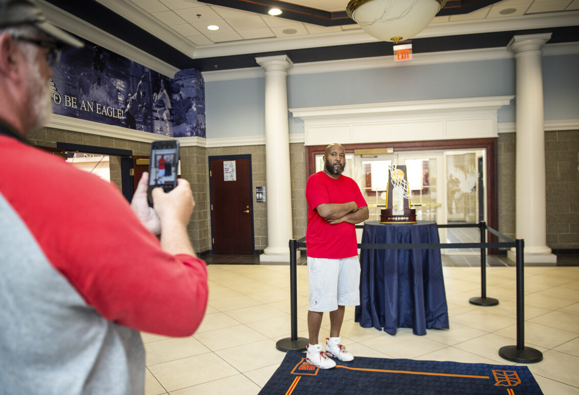 A man stands beside a basketball trophy while someone takes his photo