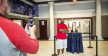 A man stands beside a basketball trophy while someone takes his photo