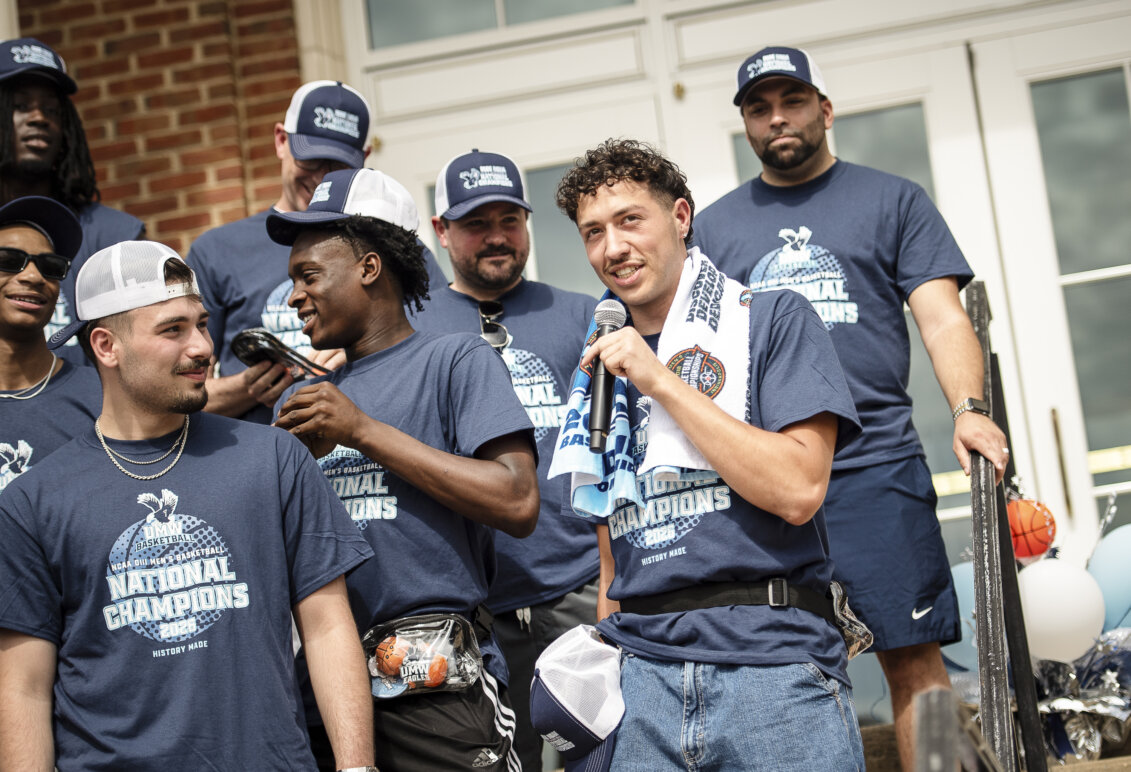 A team of basketball players, with one player speaking into a microphone