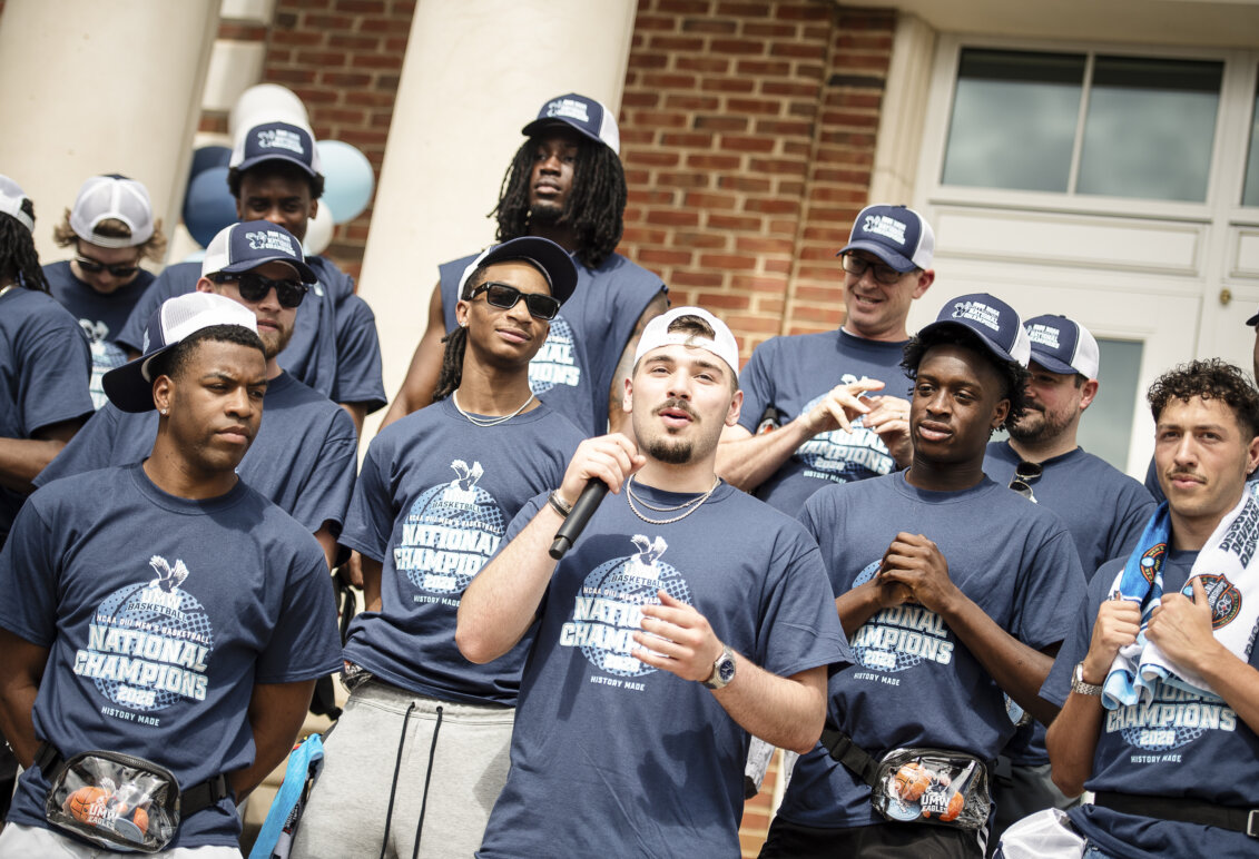 A team of basketball players, with one player speaking into a microphone